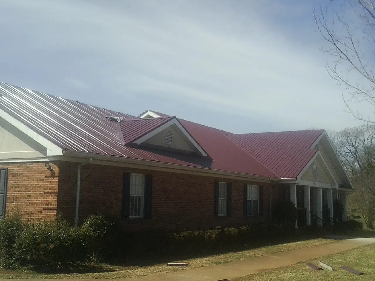 Red metal roof with gabled entries on a long brick building, from a Hail Damage Roof Repair job in Woodstock Valley