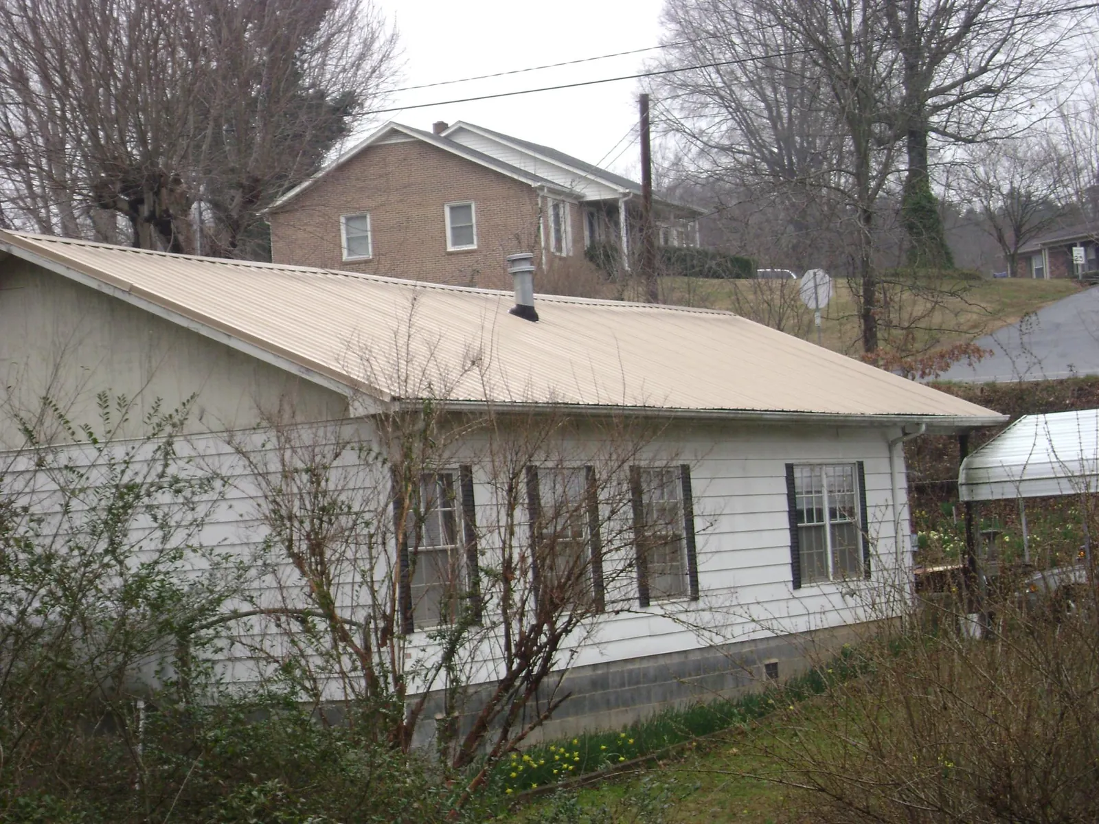 Tan metal roof on a white sided house set into a hillside — Commercial Roofing by Roofing Brothers in Woodstock Valley
